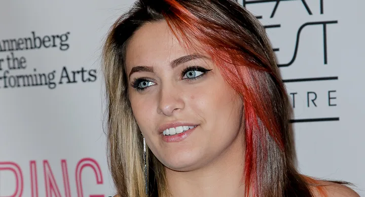 Woman with multi-colored hair at an event, standing in front of a backdrop with text.