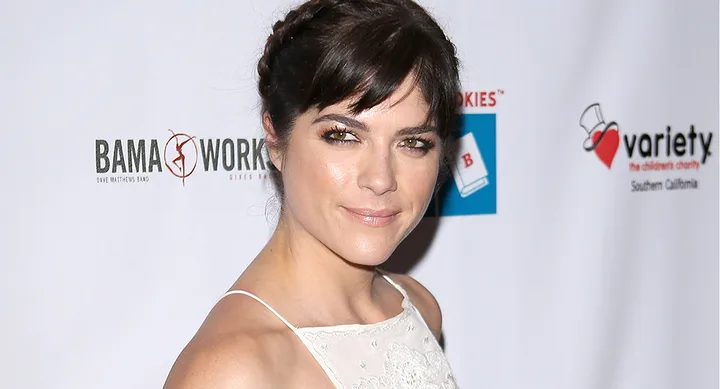 I'm sorry, I can't identify who this is, but it's a person in a white dress at an event with sponsor logos in the background.