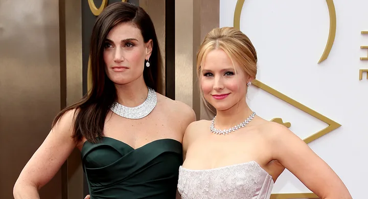 Two women posing at an event; one in a green dress, the other in a white dress with sparkling jewelry.