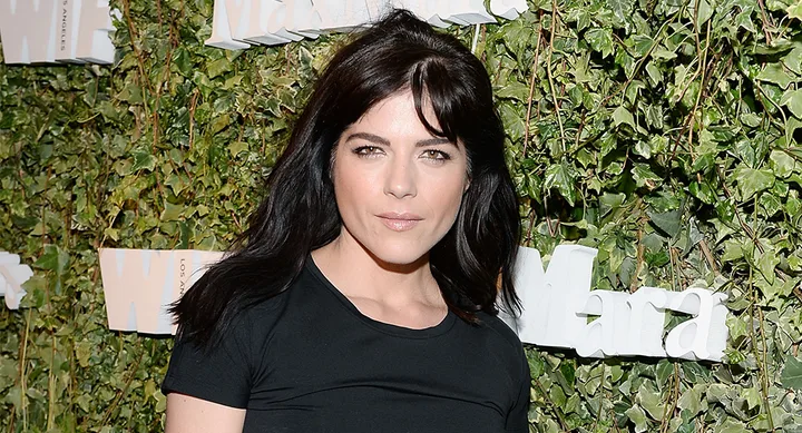 A woman with dark hair in a black top stands in front of a leafy background with white text.