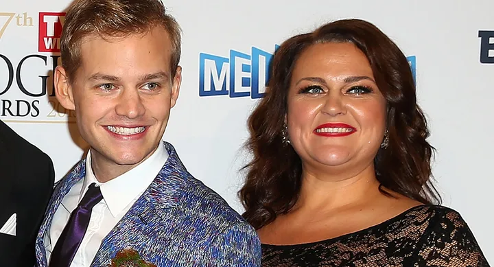 Two people smiling at an event, with a backdrop featuring logos and text.
