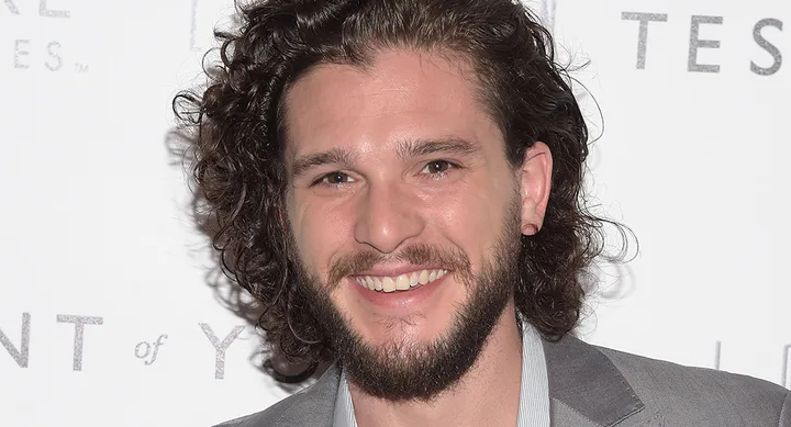 A person with long curly hair and a beard, smiling while attending an event.