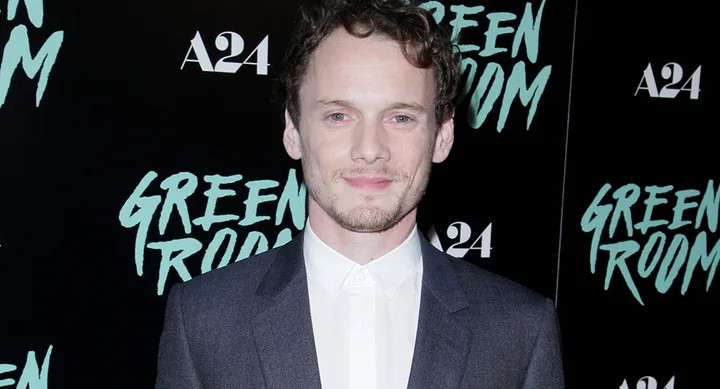 Man in suit at "Green Room" premiere with A24 logos in background.
