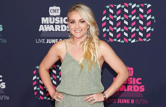 A woman in a green dress poses on the red carpet at the CMT Music Awards, with branded logos in the background.