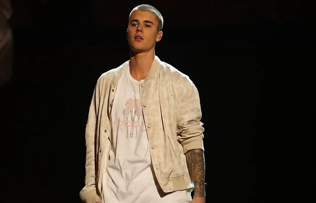 Singer performing on stage wearing a light jacket and printed shirt.