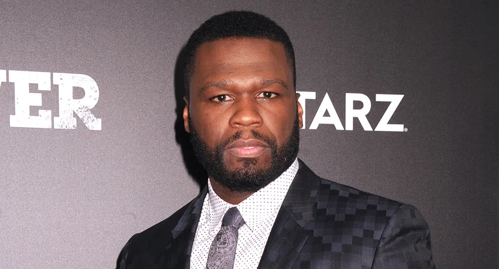 Man in a patterned suit at a "Power" event, standing in front of a dark backdrop with logos.