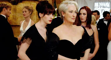 Elegant women in black dresses at a formal event, with guests mingling in the background.