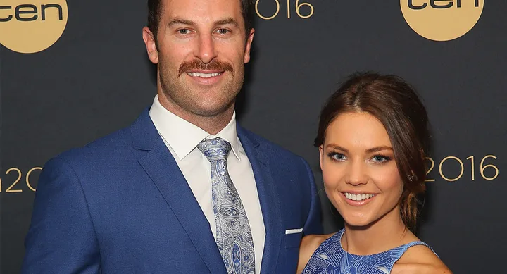 A man and woman smiling at a formal event in front of a backdrop with "ten" logos, both dressed in blue.