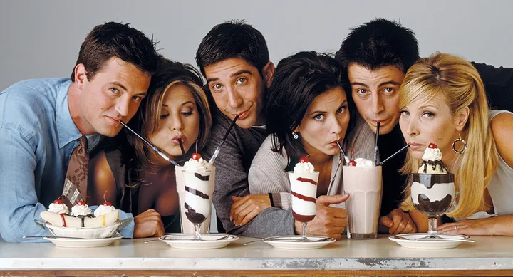 A group of people leaning over a table, sipping milkshakes and sundaes through straws.