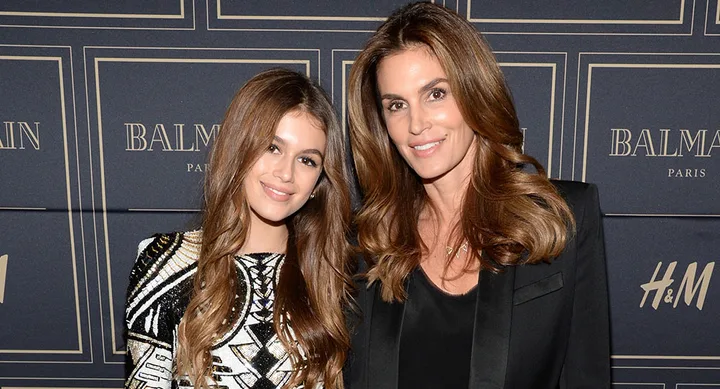 Two women smiling at a Balmain and H&M event backdrop, one in patterned dress, the other in a black blazer.