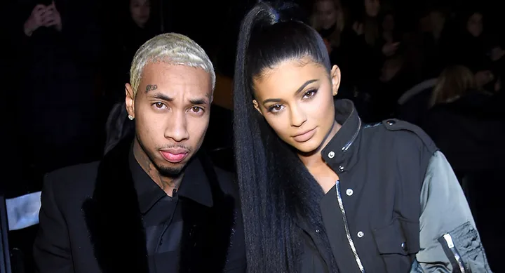 A man with dyed hair and a woman with a high ponytail pose together in stylish outfits at an event.