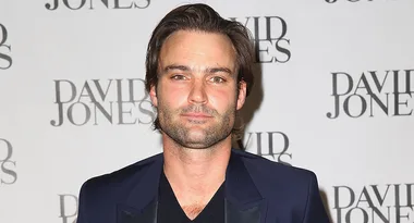 Man in a navy suit poses at the David Jones event, standing against a backdrop with the brand's logo.