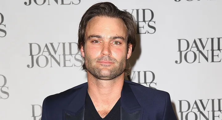 Man in a navy suit poses at the David Jones event, standing against a backdrop with the brand's logo.