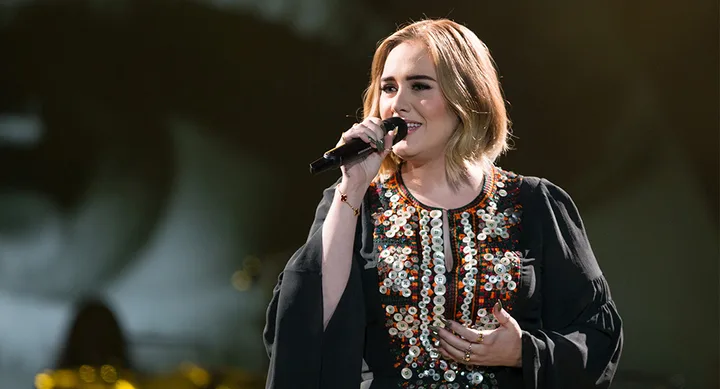 Singer performing on stage, wearing an embroidered dress, holding a microphone, and singing passionately.