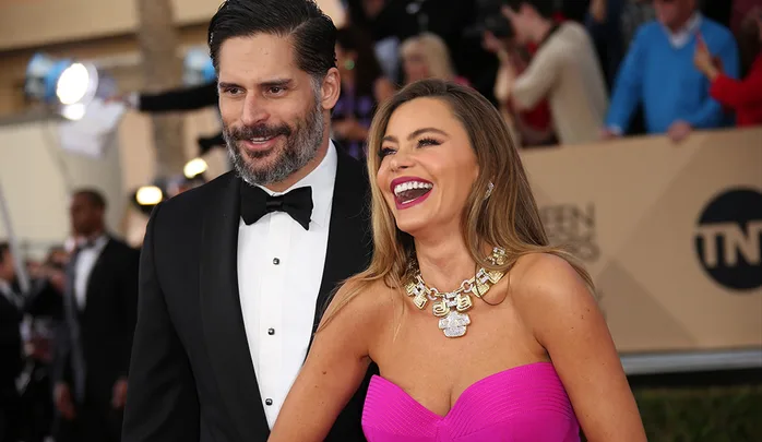 A couple in formal attire smiles cheerfully on a red carpet event.