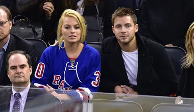 Hockey game audience, woman in blue jersey with "30", man beside her, other spectators in background.