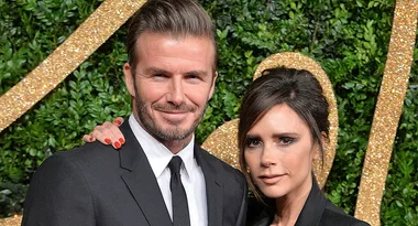 Couple in formal attire, smiling in front of a lush, decorative backdrop.