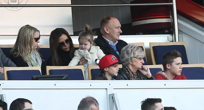 A group of people, including a woman holding a child, sitting in a stadium box, watching an event.
