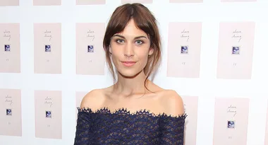 Woman in an off-shoulder navy dress poses in front of a wall with book covers featuring "alexa chung it."