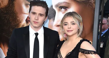 Two people pose together in formal attire at a movie premiere, with a poster in the background.