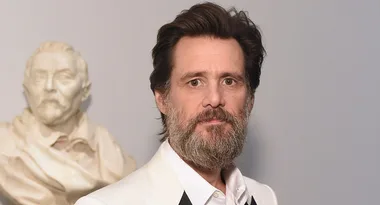 I don't know who this person is. A bearded man in a white suit stands in front of a statue bust.