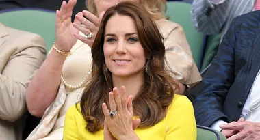 A woman in a yellow dress clapping at a sports event, surrounded by applauding spectators.