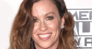 ```plaintext
Smiling woman with wavy brown hair, wearing earrings, standing in front of a white background.
```