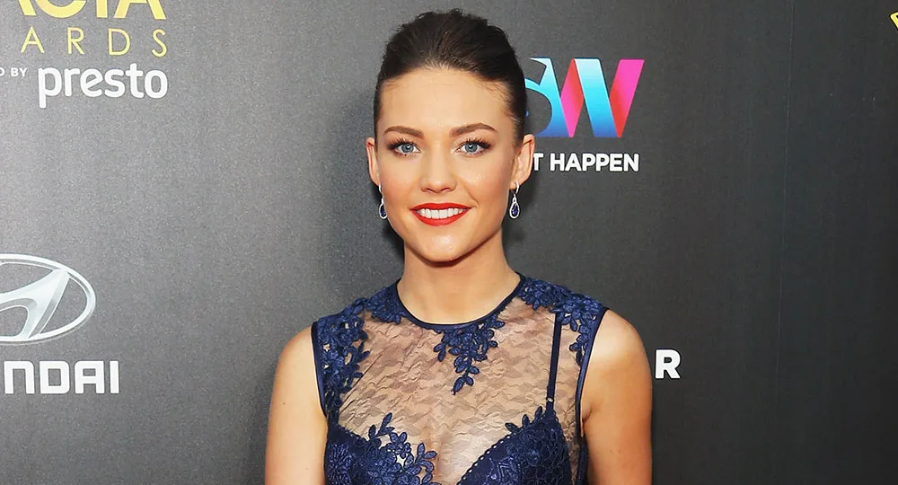 "Person in blue lace dress at awards event, smiling with dark background."