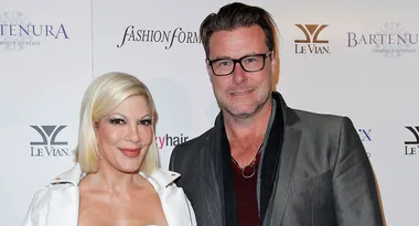 Man and woman posing together at a fashion event; logos visible in the background.