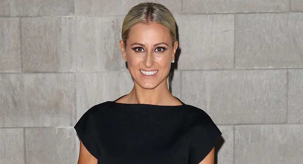 Woman in a black dress smiling in front of a gray tiled wall.