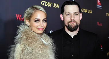 Two people posing at the G'Day USA event, one wearing a fur coat and the other in a black shirt.