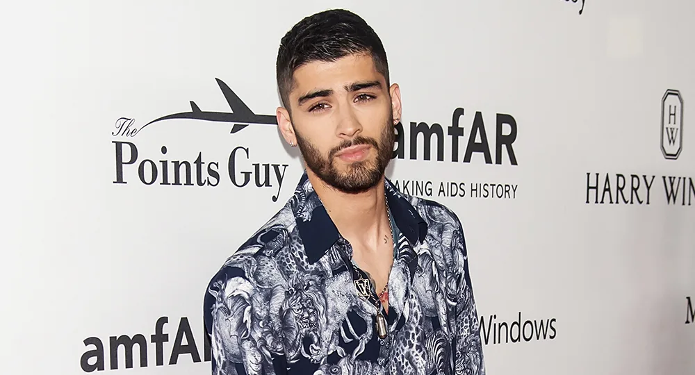 Person in a patterned shirt at an amfAR event, standing against a backdrop with logos including "The Points Guy."
