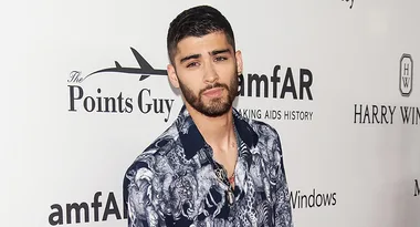 Person in a patterned shirt at an amfAR event, standing against a backdrop with logos including "The Points Guy."