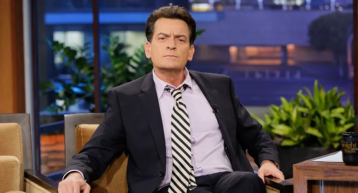 Man in a suit and striped tie sitting on a talk show set.