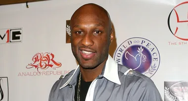 Man smiling at a red carpet event, standing in front of a logo-filled backdrop.