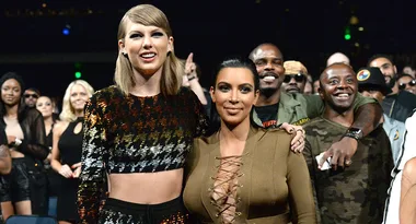 Two women smiling, surrounded by a crowd at an event, with people posing in the background.