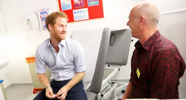 Two men sitting, smiling and talking in a brightly lit room, with medical equipment in the background.