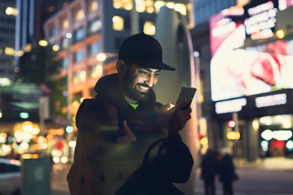 Happy man on iPhone under bright city lights
