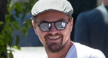 Man wearing a flat cap and sunglasses, smiling outdoors.
