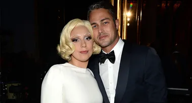 Two people posing together, one with short blonde hair in a white dress, the other in a suit with a bow tie.