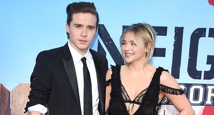 Young man in a suit and woman in a black dress posing together at a movie premiere.
