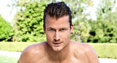 Shirtless man with wet hair outdoors, background of greenery and blurred shrubs.