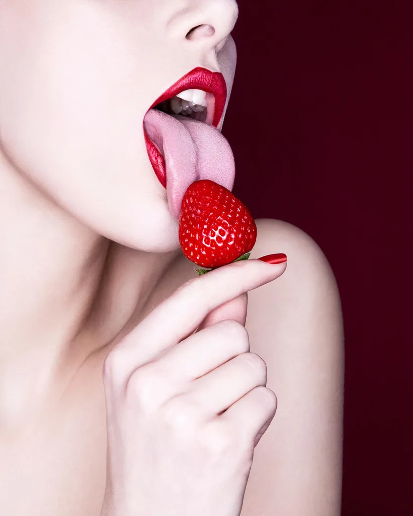 Woman holding and licking red strawberry