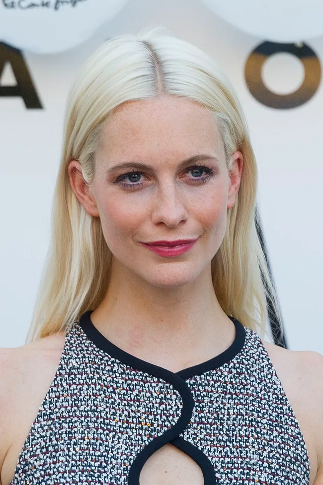 A woman with long blonde hair wearing a patterned sleeveless top at an event.