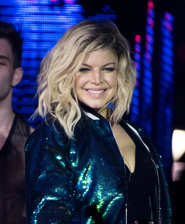 Singer performing on stage in a shimmering jacket with a colorful background.