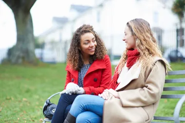 Two girls sitting on a bench in a parkl
