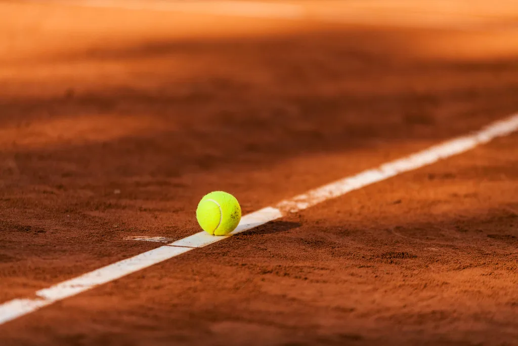 Yellow tennis ball sitting on a red dirt tennis court