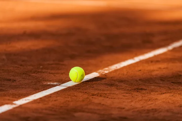 Yellow tennis ball sitting on a red dirt tennis court