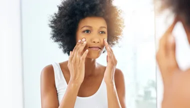 Lady rubbing cream into her temples in mirror