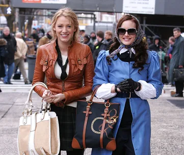 Two women in stylish outfits with handbags, smiling on a busy street.